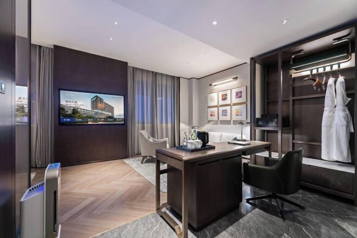 Ein modernes Hotelzimmer mit Flachbildfernseher, Schreibtisch mit Stuhl, begehbarem Kleiderschrank und großem Fenster mit Vorhängen.