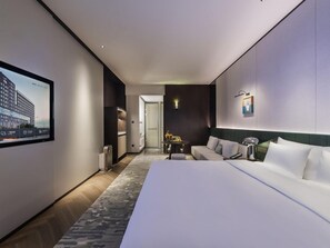 A modern hotel room with a large bed, a seating area, a television, and a door leading to the bathroom. - Novotel Xian Xixian (Xianyang)