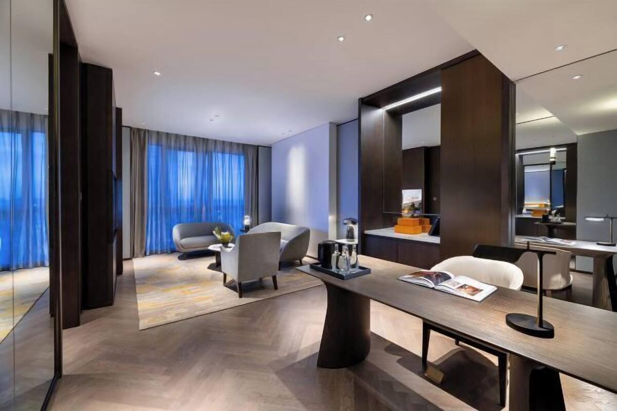 Ein modernes Hotelzimmer mit großem Schreibtisch, bequemen Sitzgelegenheiten, einem großen Spiegel und Blick auf die Stadt.