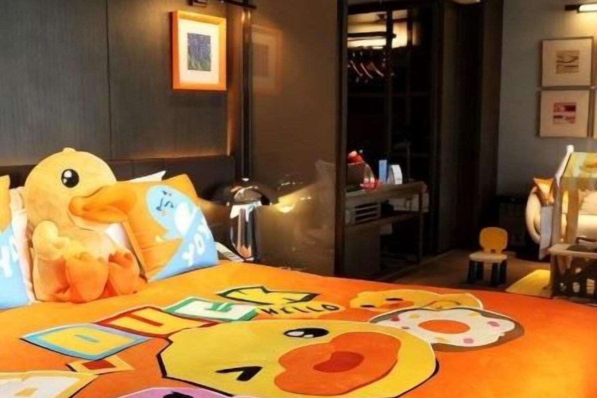 Habitación de hotel con una cama decorada con diseños de personajes de caricaturas, un espejo grande y vistas a un pasillo con una puerta.