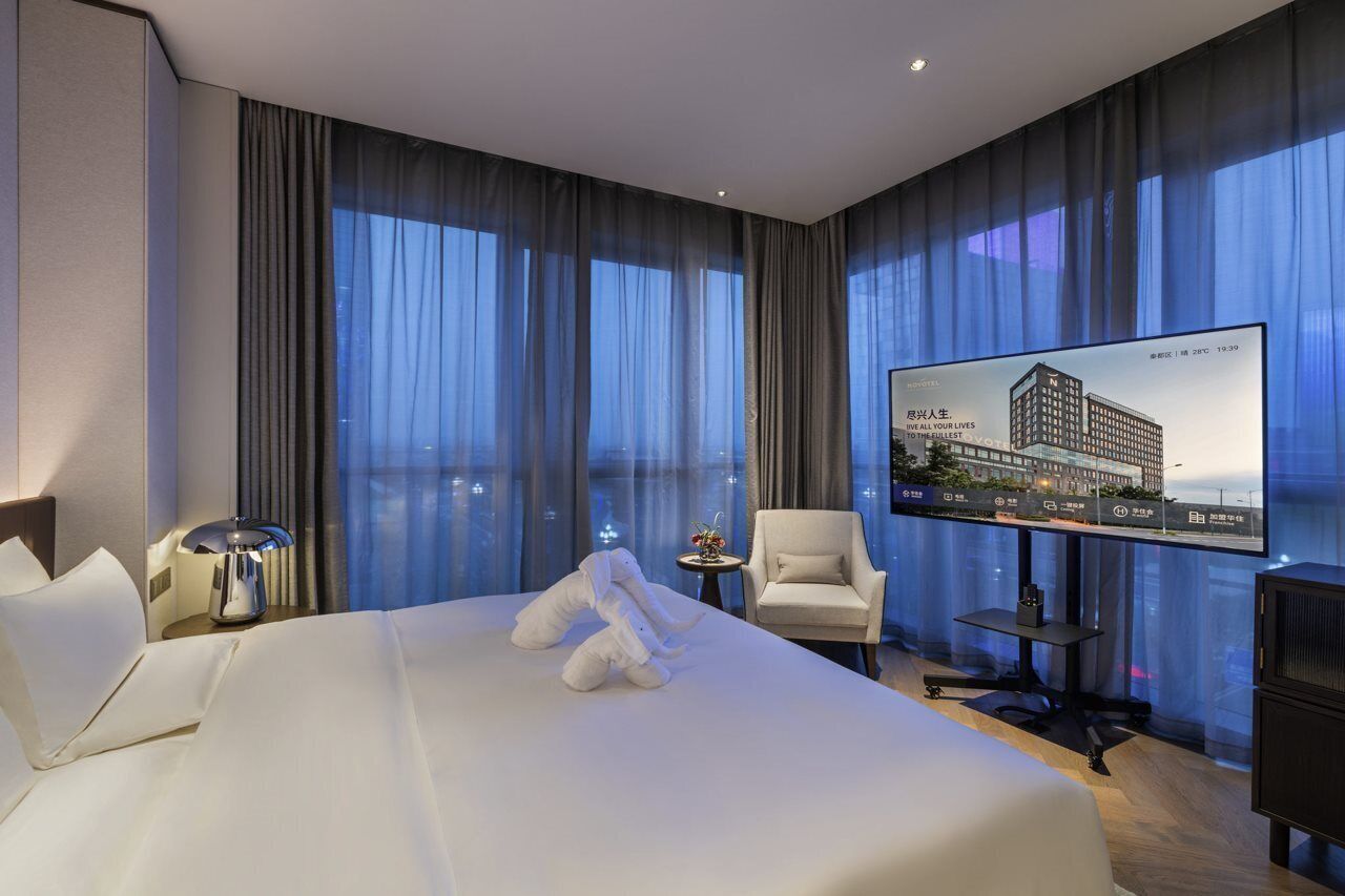A hotel room with a large bed, a television, a chair, and a small table.