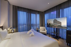 A hotel room with a large bed, a television, a chair, and a small table. - Novotel Xian Xixian (Xianyang)