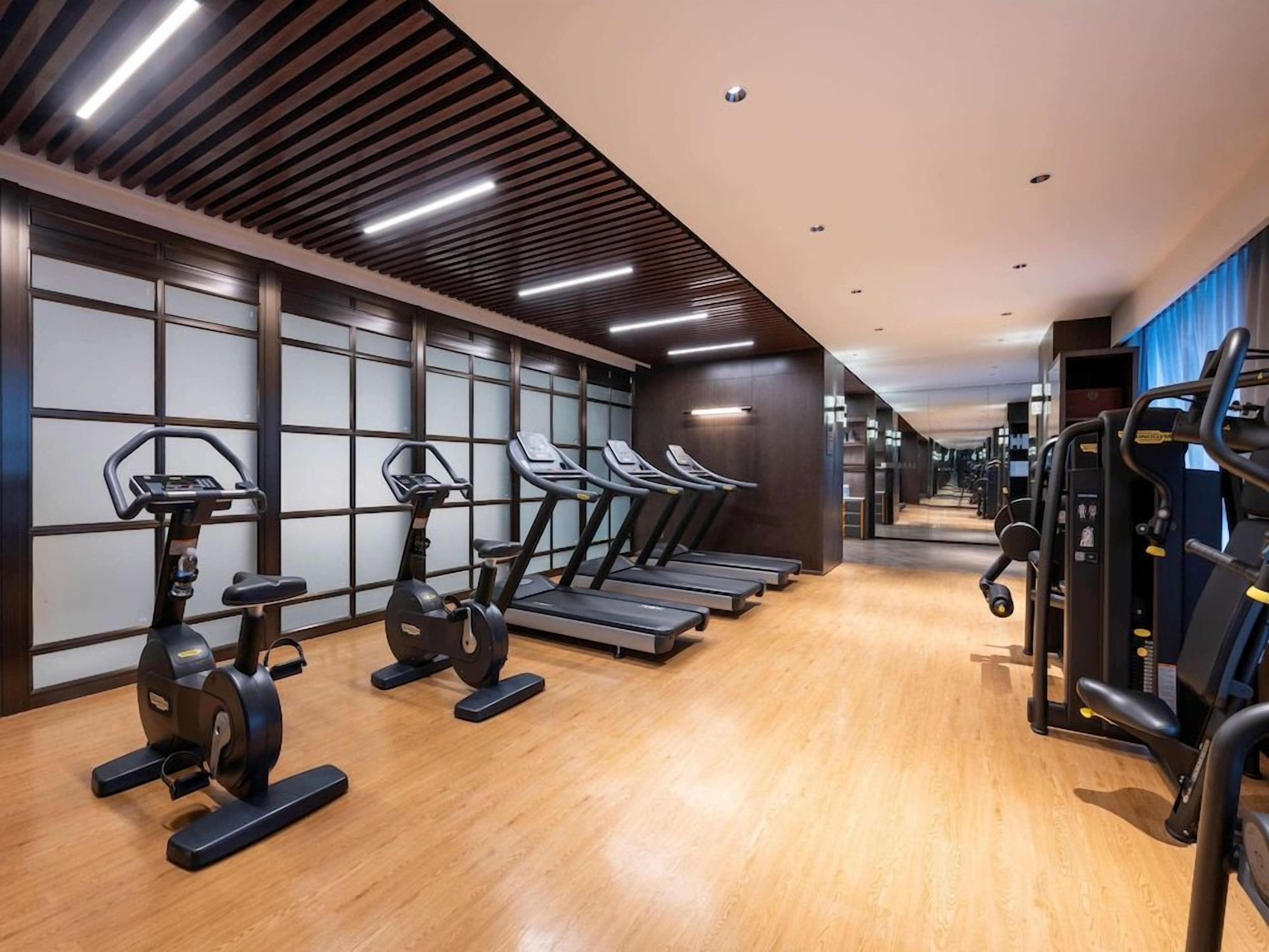 A gym with exercise equipment, including treadmills and stationary bikes, and a wooden floor.