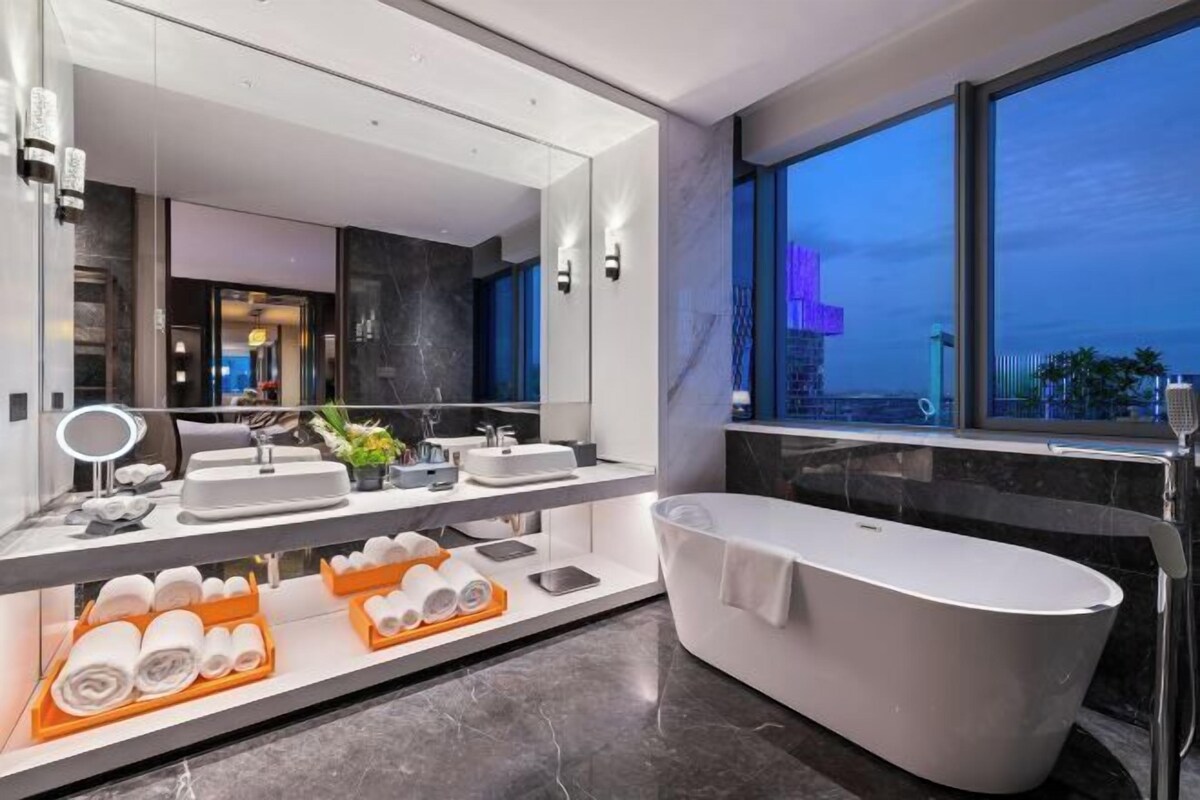 Un baño moderno con una bañera independiente, un espejo grande y un tocador con varios lavabos.