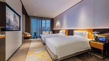 A hotel room with a large bed, a desk, a chair, a bedside table with a lamp, and a TV mounted on the wall.