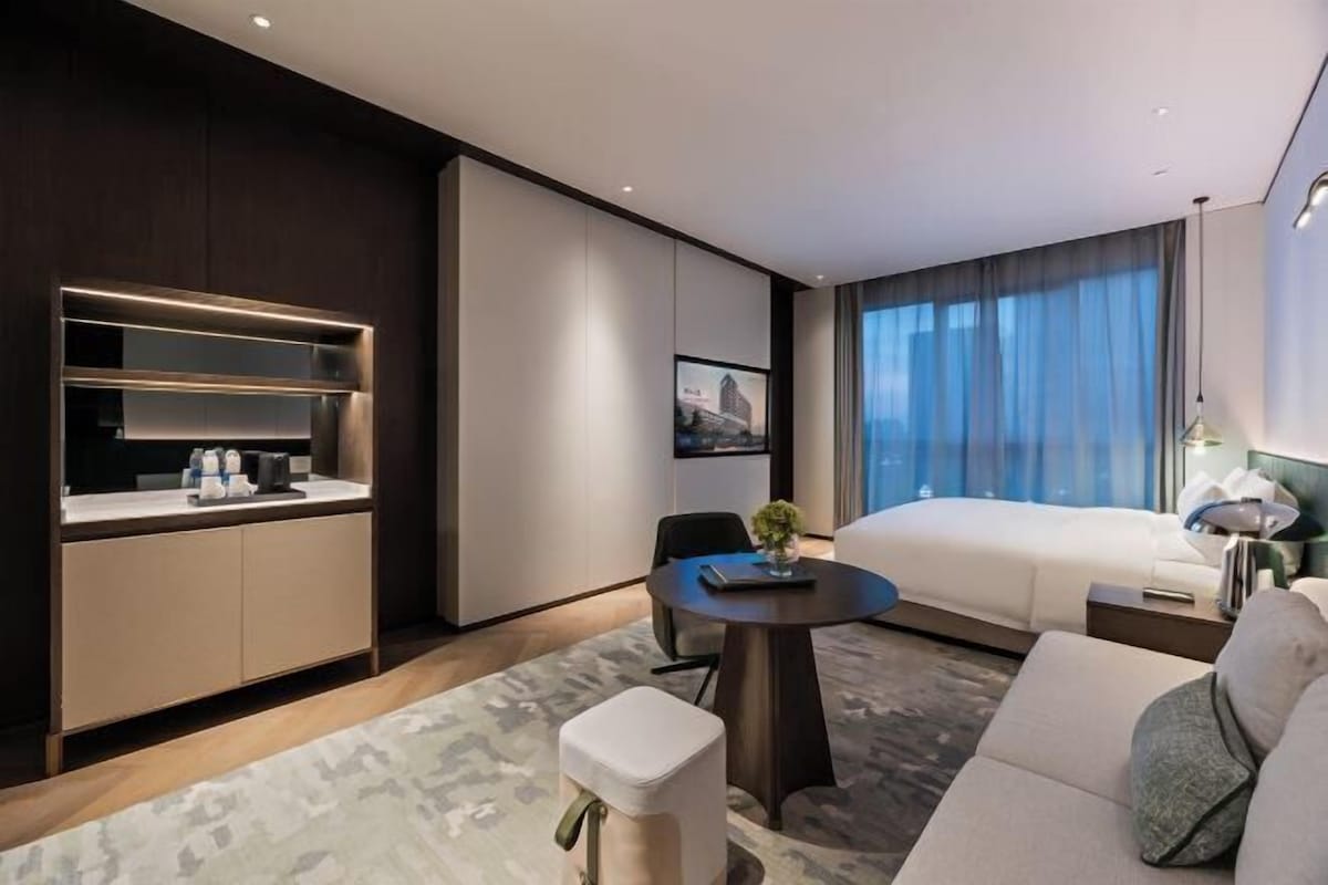 Una habitación de hotel moderna con cama, sofá, mesa de comedor y kitchenette.
