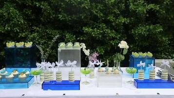 Ein Tisch mit verschiedenen Speisen und Getränken, darunter Cupcakes, Desserts und Cocktails, auf einer weißen Tischdecke.