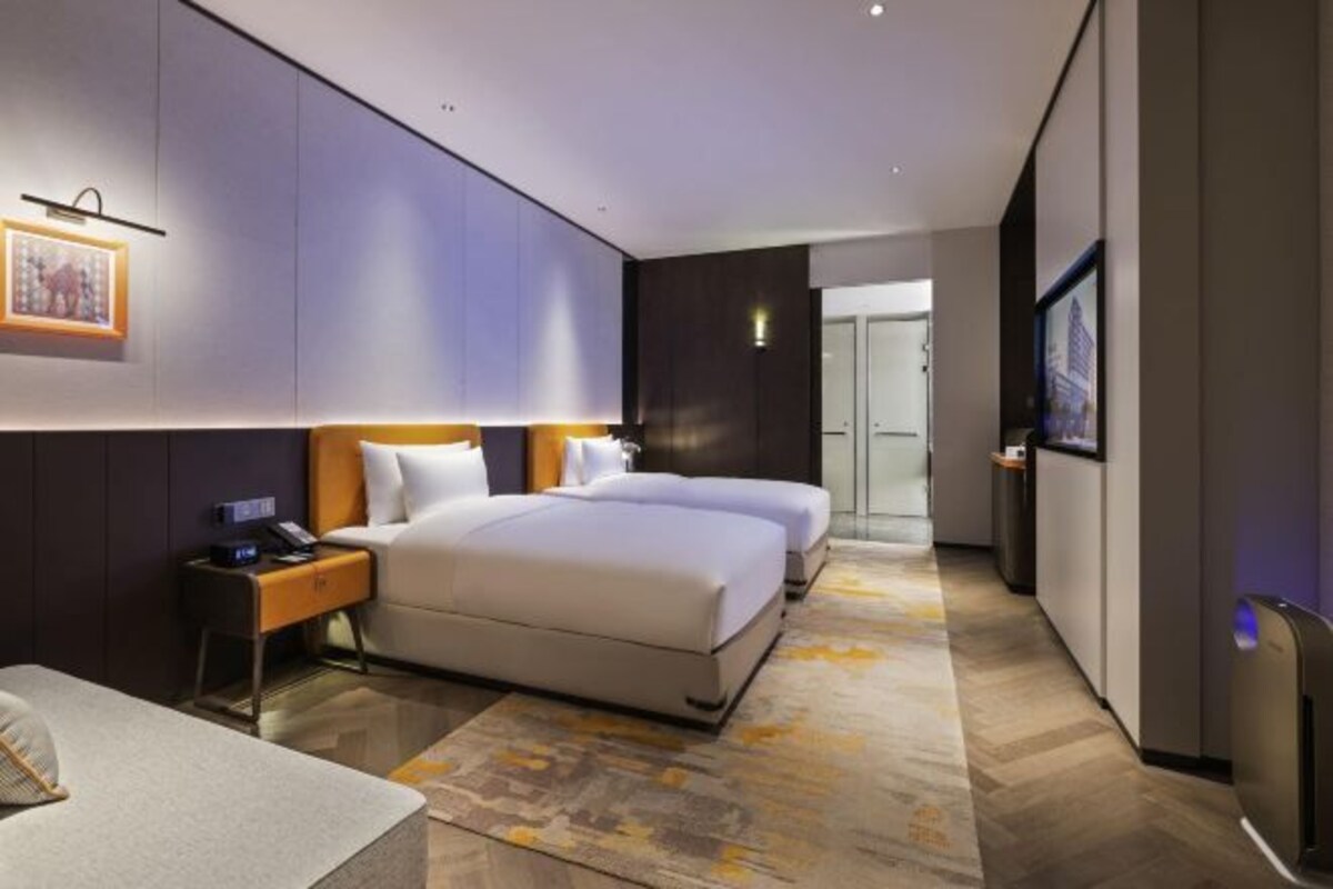 Habitación de hotel moderna con una cama grande, mesitas de noche y vistas al pasillo.