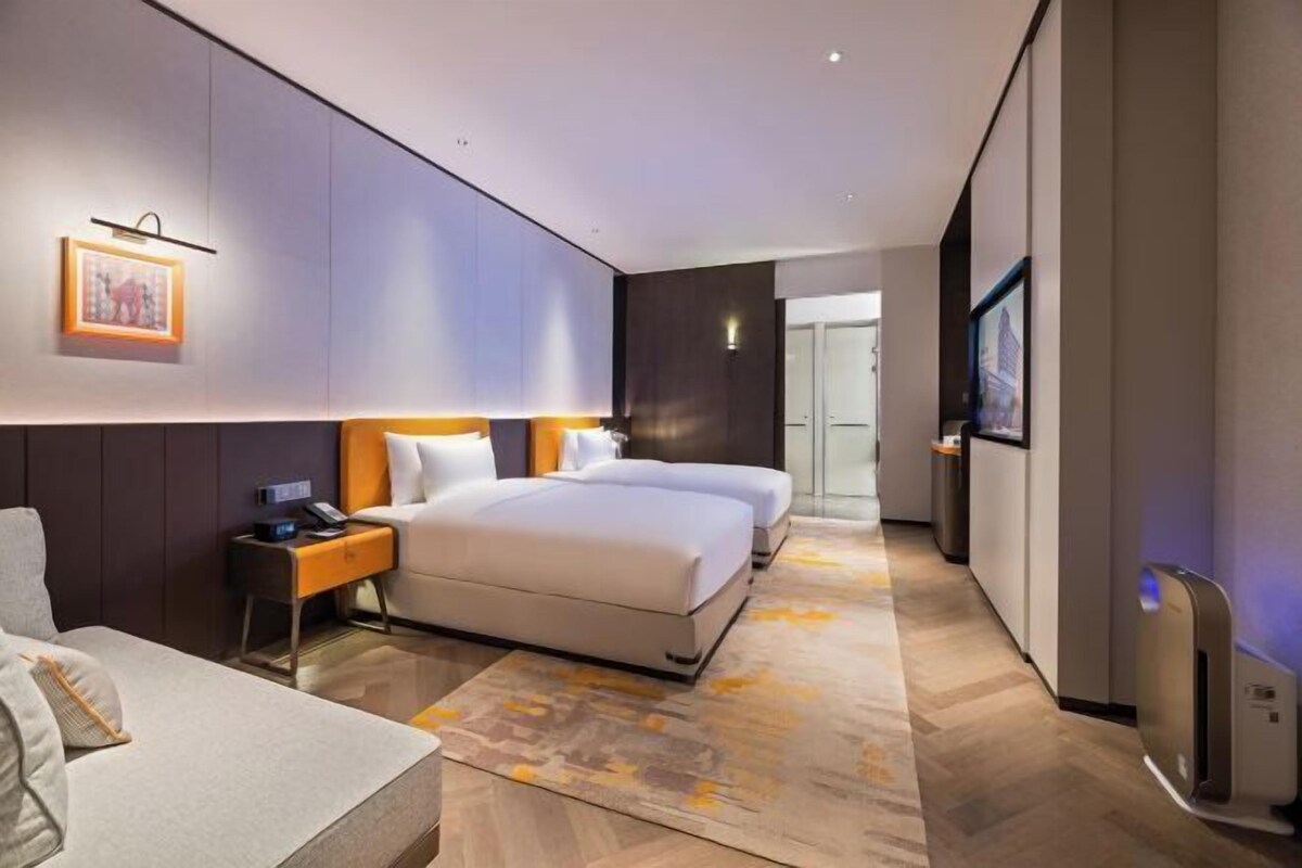 Una habitación de hotel moderna con una cama grande, mesitas de noche, un sofá y vistas a la ciudad.