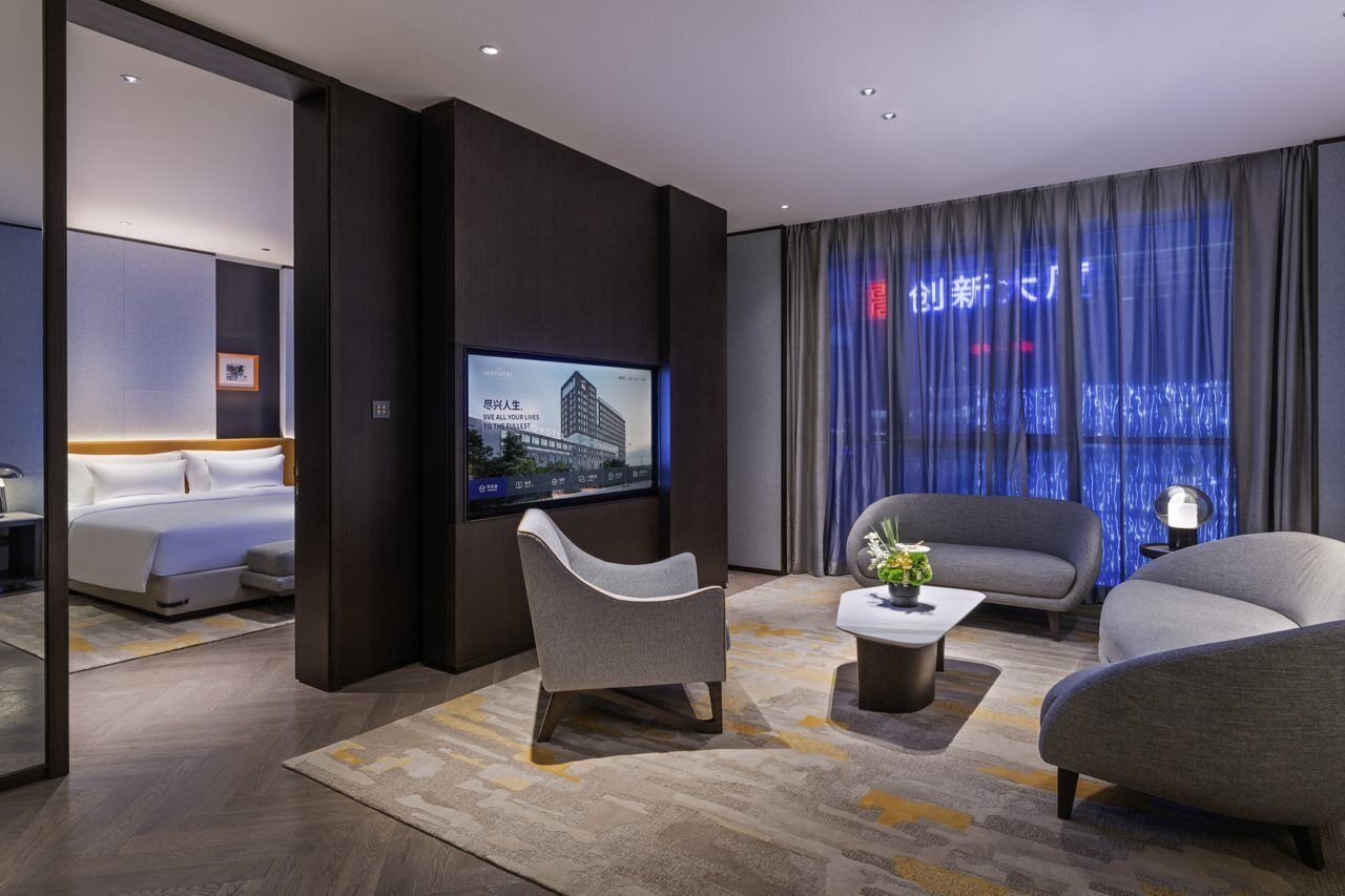 A modern hotel room with a bed, a flat-screen TV, a sofa, and a coffee table.