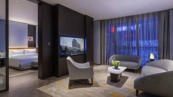 A modern hotel room with a bed, a flat-screen TV, a sofa, and a coffee table.