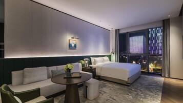 A modern hotel room with a bed, sofa, and a small table with a lamp.