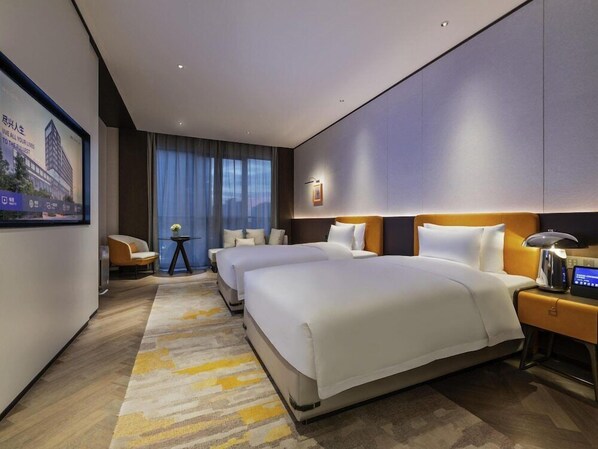 Habitación de hotel con una cama grande, una mesita de noche con lámpara, una pequeña mesa con un jarrón y un ventanal con cortinas.