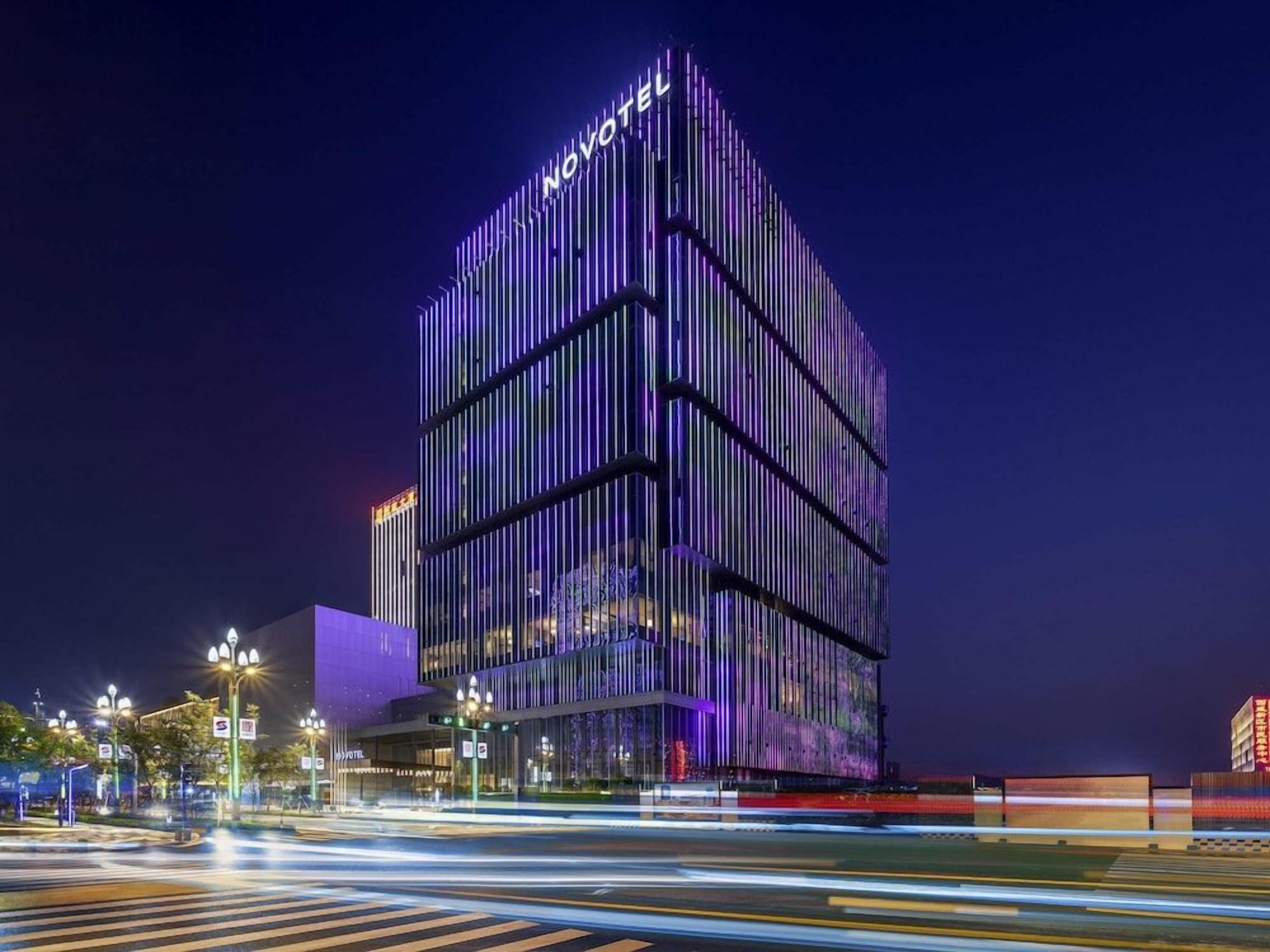 Un hôtel moderne, reconnaissable à son grand panneau « NOVOTEL », qui se distingue par sa façade verticale originale et son entrée bien éclairée.