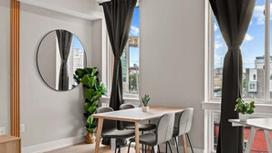 A modern room with a dining table, chairs, a mirror, and large windows with curtains. - Luxury Studio | 1 Bed | Northern Liberties (Philadelphia)
