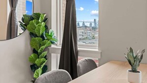 A room with a dining table, chairs, a potted plant, a mirror, and a window with curtains. - Luxury Studio | 1 Bed | Northern Liberties (Philadelphia)