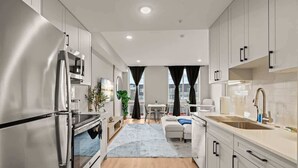 A modern kitchen with stainless steel appliances, a dining area with a table and chairs, and a living space with a sofa and a coffee table. - Luxury Studio | 1 Bed | Northern Liberties (Philadelphia)