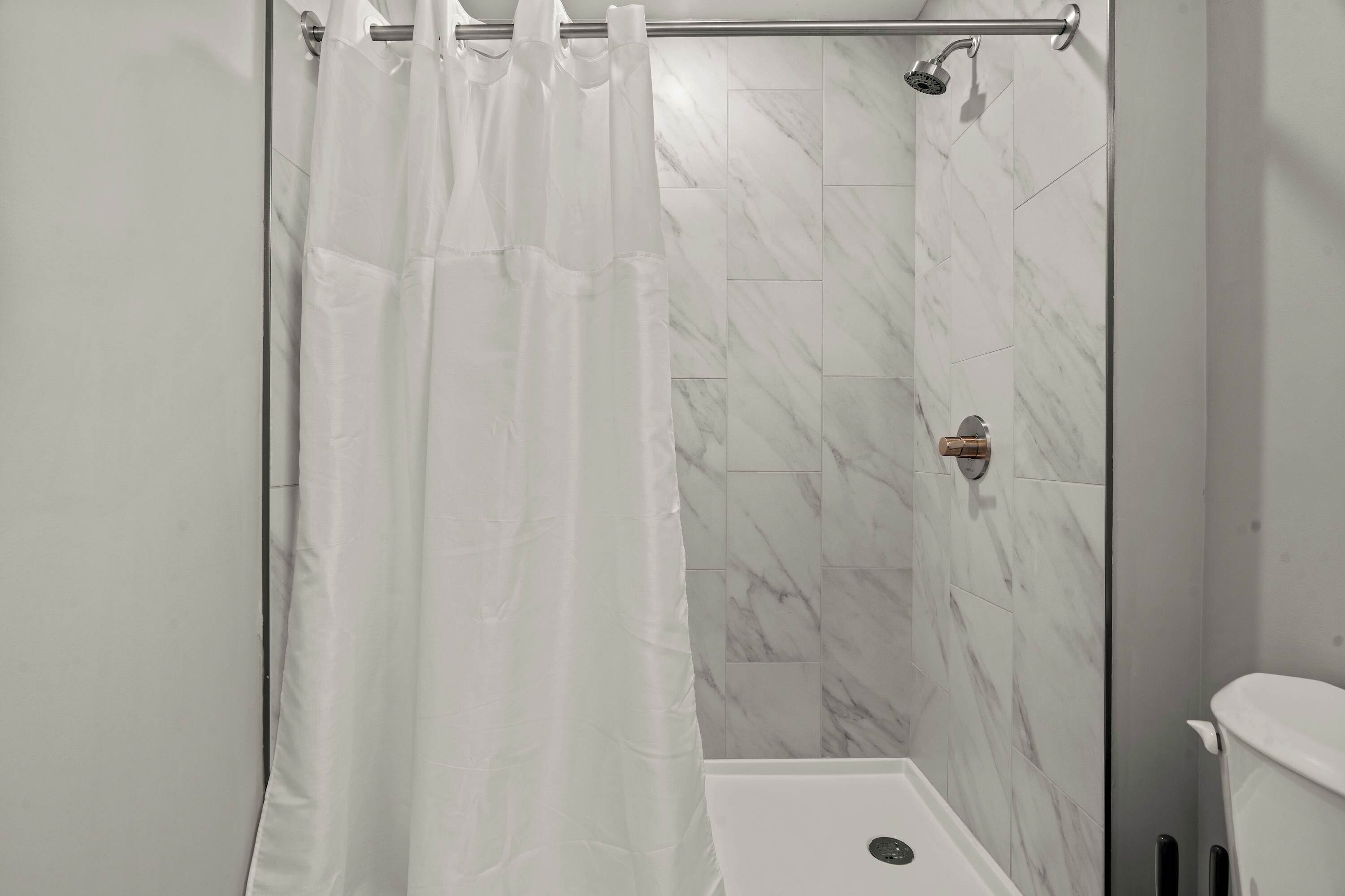 A shower area with a white curtain, a handheld showerhead, and a toilet.