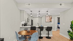 A modern kitchen with a central island, a dining area with a round table and chairs, and a living space with a bed and a plant.