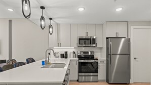 A modern kitchen with white cabinetry, stainless steel appliances, and pendant lighting. - Chic Waterfront Pad | Sleeps 8 | Prime 2BR Getaway (Philadelphia)