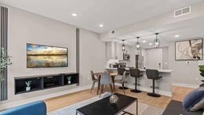 A modern living room with a blue sofa, a coffee table, and a painting of a sunset. - Chic Waterfront Pad | Sleeps 8 | Prime 2BR Getaway (Philadelphia)