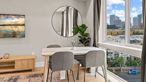 A modern dining area with a large window, a round mirror, and a painting on the wall. - Luxury Studio | 1 Bed | Northern Liberties (Philadelphia)