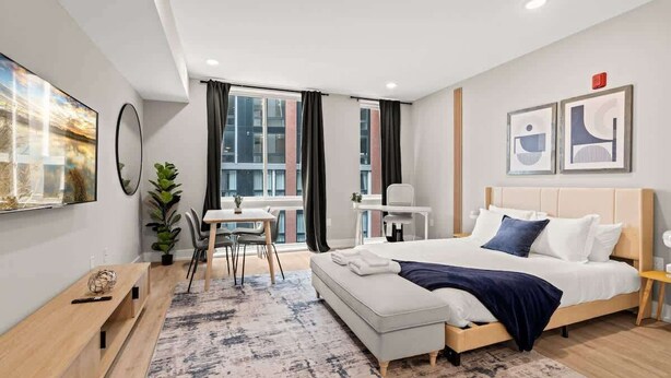 A modern hotel room with a large bed, a desk, and a view of the city. - Luxury Studio | 1 Bed | Northern Liberties (Philadelphia)