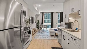 A modern kitchen with stainless steel appliances, a dining area with a table and chairs, and a view of the city through large windows. - Luxury Studio | 1 Bed | Northern Liberties (Philadelphia)