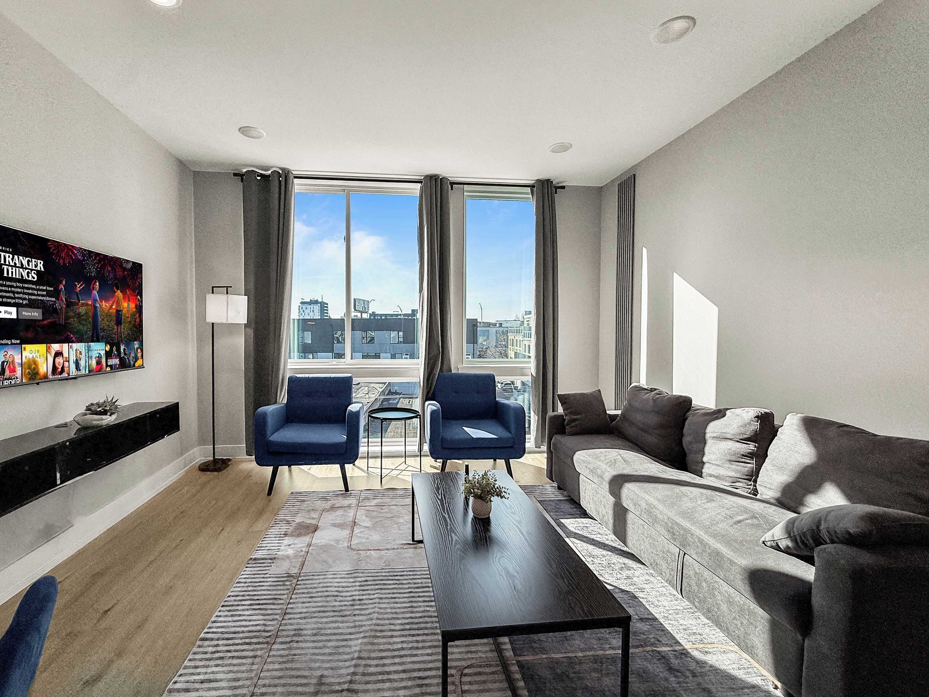 A modern living room with a sofa, two armchairs, a coffee table, and a TV mounted on the wall.