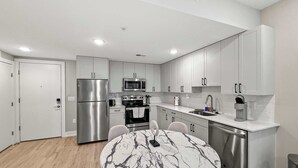 A modern kitchen with stainless steel appliances, a marble dining table, and light-colored cabinetry. - Luxury 1BD | 2 Beds | Northern Liberties (Philadelphia)