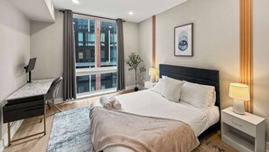 A modern hotel room with a large bed, a desk, and a window with a city view. - Luxury 1BD | 2 Beds | Northern Liberties (Philadelphia)