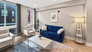A modern living room with a blue sofa, a white armchair, a coffee table, and a floor lamp. - Luxury 1BD | 2 Beds | Northern Liberties (Philadelphia)