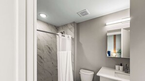 A modern bathroom with a marble wall, a white toilet, a shower with a white curtain, and a mirror above the sink. - Luxury 1BD | 2 Beds | Northern Liberties (Philadelphia)