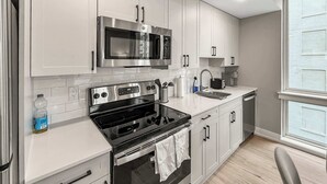 A modern kitchen with white cabinets, stainless steel appliances, and a window providing natural light. - Luxury 1BD | 2 Beds | Northern Liberties (Philadelphia)