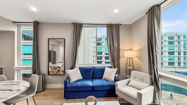 A modern living room with a blue sofa, white armchairs, a round coffee table, and a floor lamp. - Luxury 1BD | 2 Beds | Northern Liberties (Philadelphia)