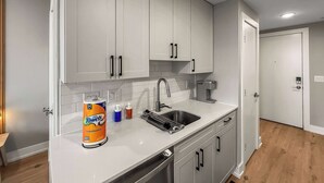 A modern kitchen with white cabinets, a stainless steel sink, and a dish rack. - Luxury Studio | 1 Bed | Northern Liberties (Philadelphia)
