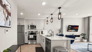 Una cocina moderna con electrodomésticos de acero inoxidable, una isla central, iluminación colgante y un televisor de pantalla plana montado en la pared.