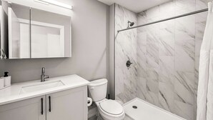 Un baño moderno con lavamanos, inodoro y zona de ducha blancos.