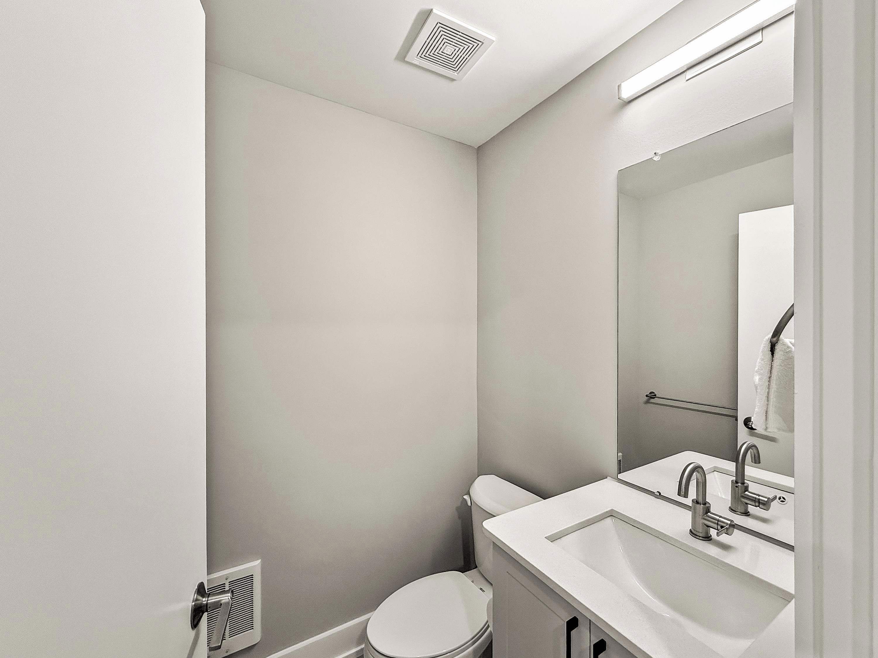 A small, clean bathroom with a toilet, sink, and mirror.
