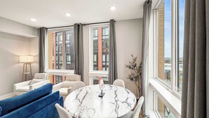A modern living room with a round marble table, two sofas, a floor lamp, and large windows with curtains.