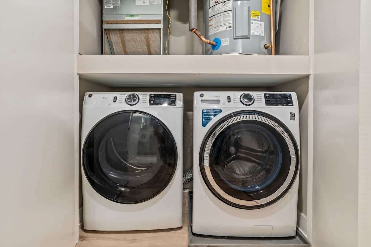 Two front-loading washing machines in a laundry room with a water heater and a utility meter above.