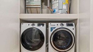 Two front-loading washing machines in a laundry room with a water heater and a utility meter above. - Luxury 1BD | 2 Beds | Northern Liberties (Philadelphia)