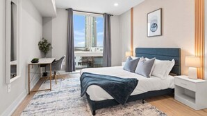 A modern bedroom with a large bed, bedside tables, a desk, and a view of tall buildings. - Luxury 1BD | 2 Beds | Northern Liberties (Philadelphia)