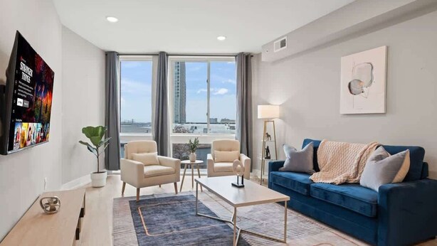 A modern living room with a blue sofa, two armchairs, a coffee table, and a TV mounted on the wall. - Luxury 1BD | 2 Beds | Northern Liberties (Philadelphia)