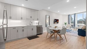 A modern kitchen with white cabinets, a dining area with a marble table, and a large window providing a view of the outdoors. - Luxury 1BD | 2 Beds | Northern Liberties (Philadelphia)