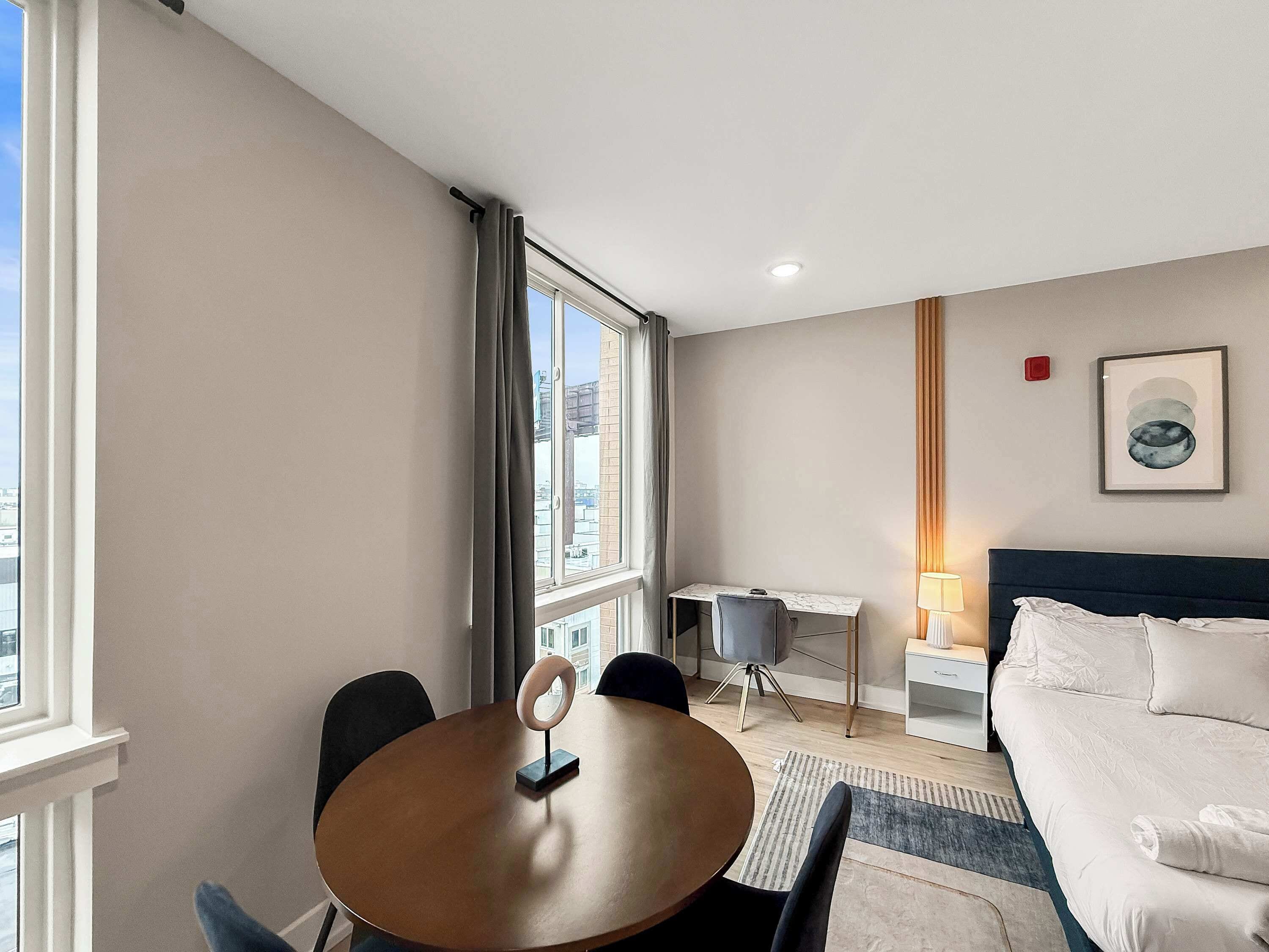 A hotel room with a bed, a desk, a chair, a table, and a window with curtains.