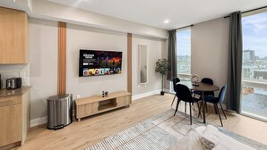 Ein modernes Wohnzimmer mit Flachbildfernseher, Holzausbau, Essbereich mit Stühlen und einem großen Fenster mit Blick auf die Stadt.