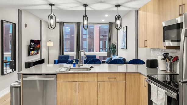 A modern kitchen with a central island, stainless steel appliances, wooden cabinets, and pendant lighting. - Luxury 2BD | 4 Beds | Northern Liberties (Philadelphia)