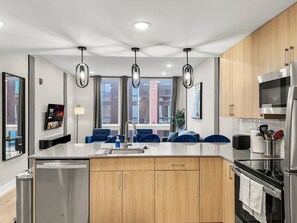 A modern kitchen with a central island, stainless steel appliances, wooden cabinets, and pendant lighting.