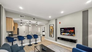 A modern living room with a sofa, blue chairs, a coffee table, and a TV wall-mounted above a fireplace. - Luxury 2BD | 4 Beds | Northern Liberties (Philadelphia)